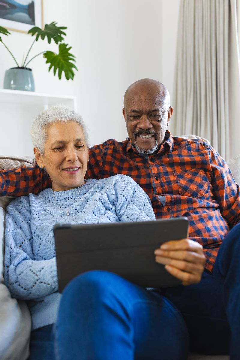 Diverse senior couple on a coach looking at a their laptop 